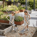 Two children gardening in a backyard with raised beds and plants using toy rake and toy shovel